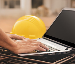 Photo montrant des mains sur un clavier d'ordinateur avec un casque jaune de techniciens en arrière plan