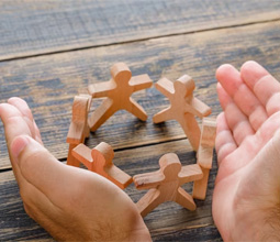 Photo de main qui regroupe des figurines en bois en forme d'humain